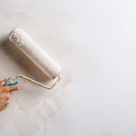 Close up photo of hand painting wall with roller in white color. Copy space.