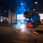 Close up view of worker welding metal construction in industrial workshop.