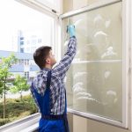 Rear View Of A Young Male Housekeeper Cleaning Window