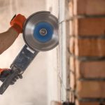 The industrial Builder works with a professional angle grinder to cut bricks and build interior walls. Professional on the construction site. The concept of electrician and handyman. House and reconstruction of the house.