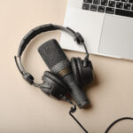 Flat lay composition with Microphone for podcasts  and black studio headphones on brown background with coffee and laptop, learning online education concept.